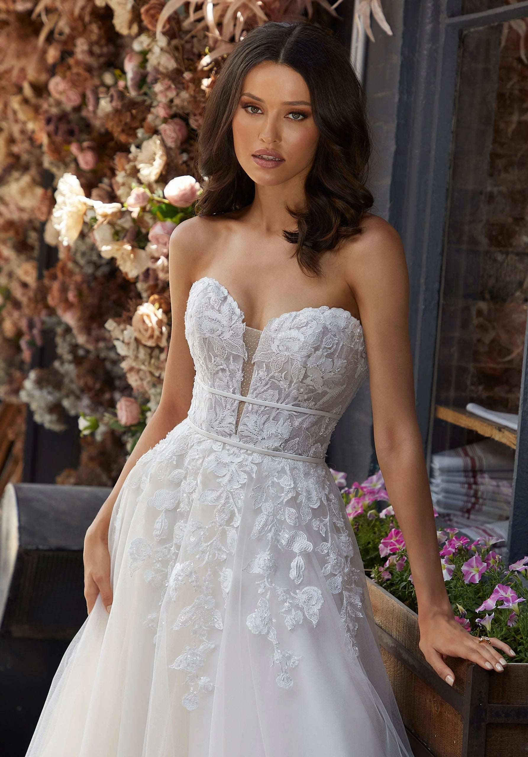 Woman wearing Judith by Morilee - a strapless wedding dress with floral details in an outdoor setting.