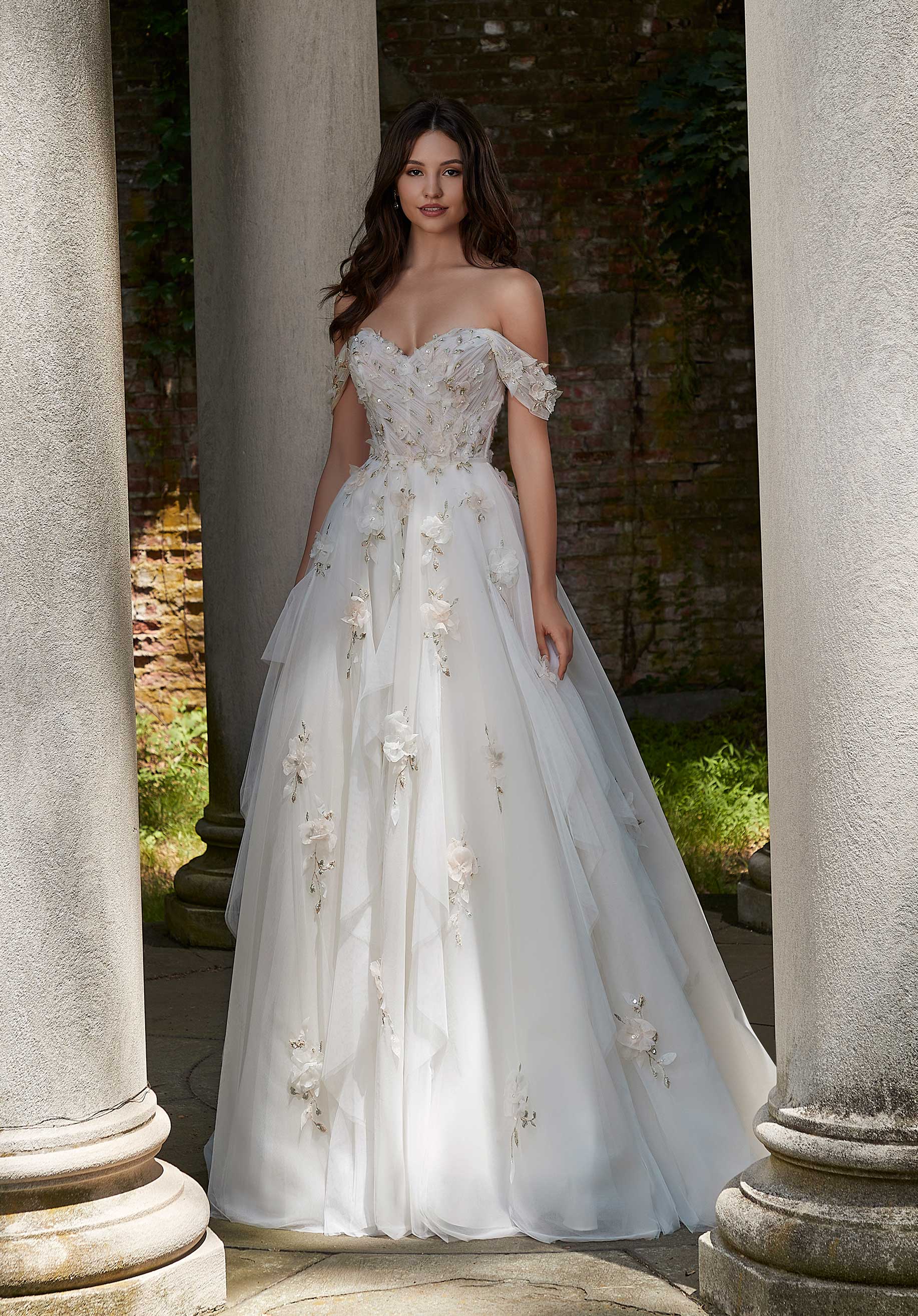 Woman in Petal by Morilee - a white floral wedding dress standing between stone columns.