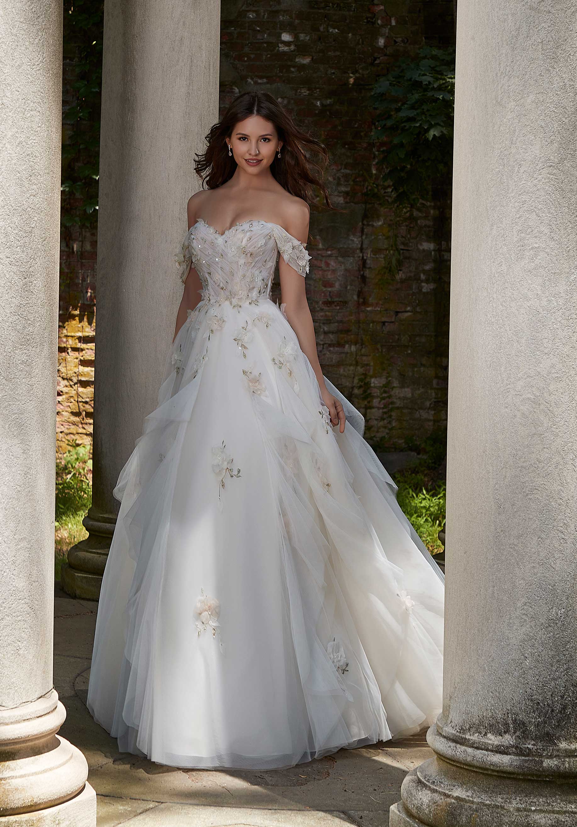 Woman in Petal by Morilee - a white wedding dress standing between stone columns.