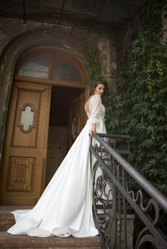 Woman in a white dress standing on a staircase with a wooden door and ivy-covered wall in the background
