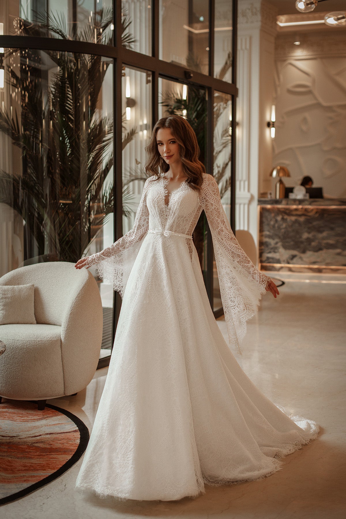 Woman in a white lace dress standing in an elegant interior setting.