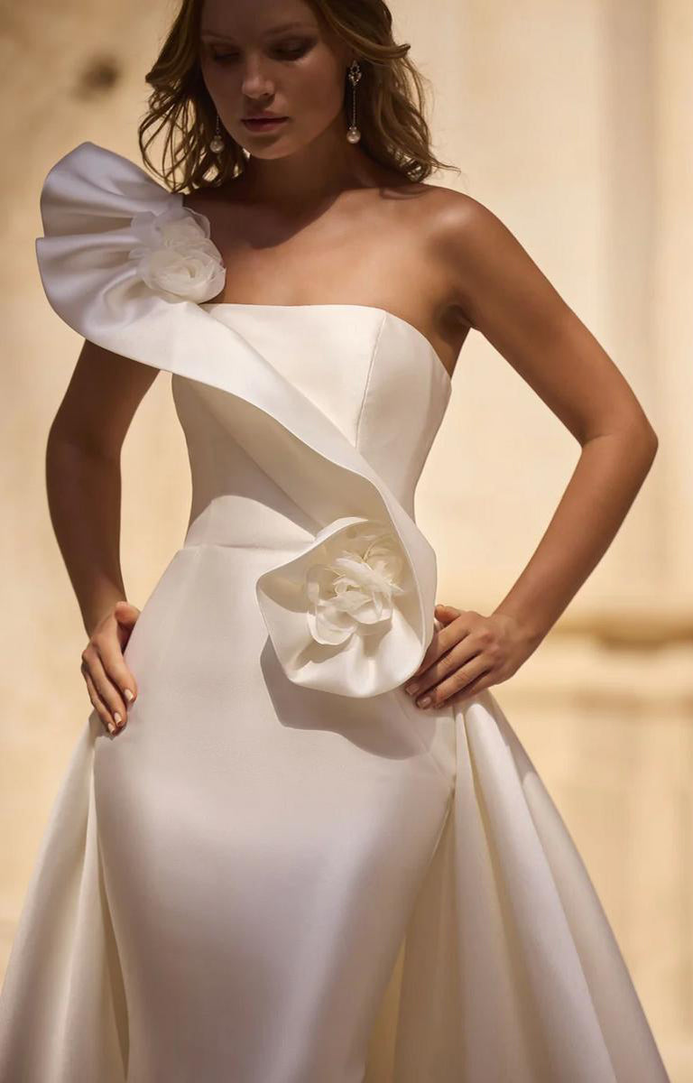 Woman wearing Veni Infantino - Hatherley 63032 – Strapless Fishtail Fit and Flare Wedding Dress against a background with a limestone wall.