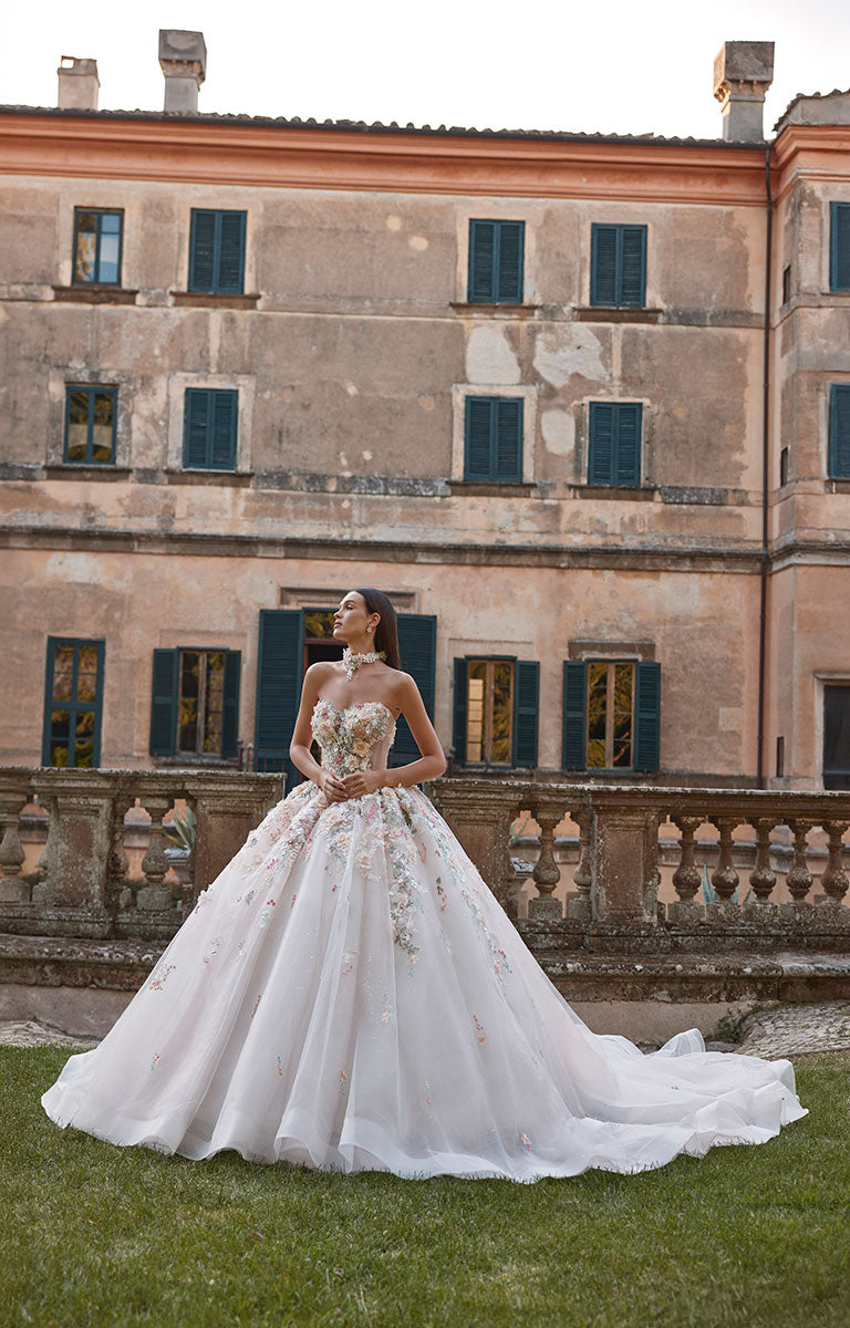 Woman in 63201A Aurora by Veni Infantino - Strapless Ball Gown Wedding Dress with 3D Floral Appliqués standing in front of an elegant building with green shutters.