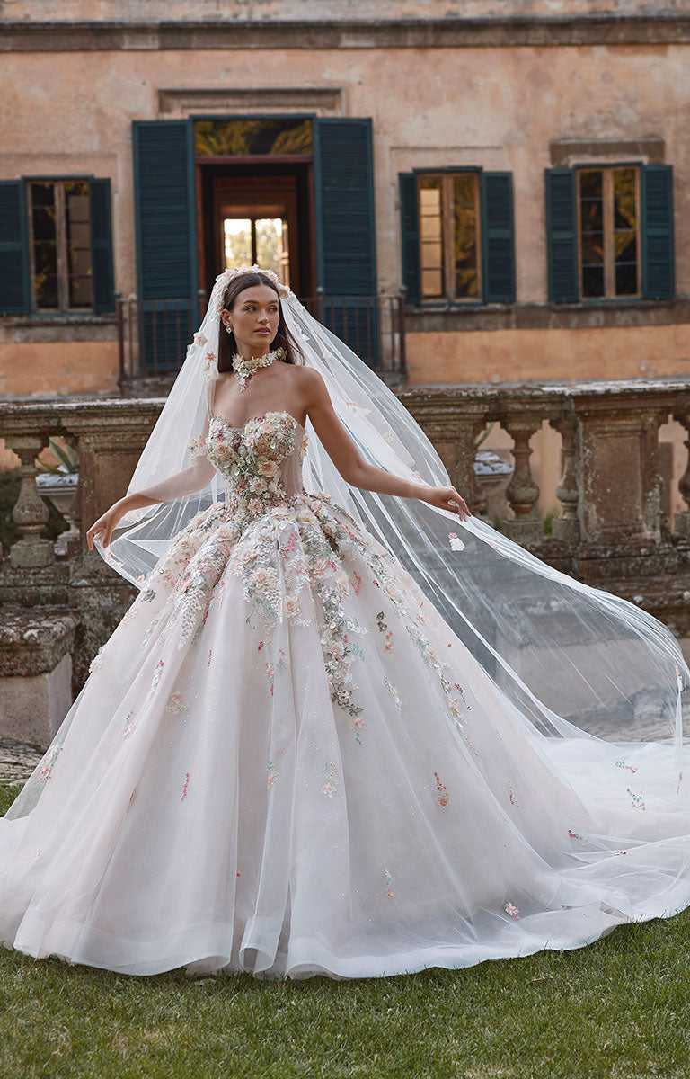 Woman in 63201A Aurora by Veni Infantino - Strapless Ball Gown Wedding Dress with 3D Floral Appliqués with a long veil standing in front of a classical building.