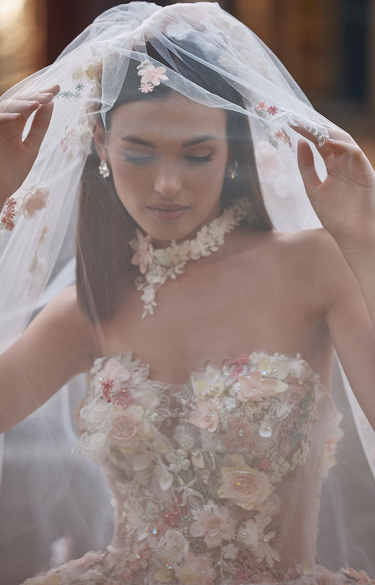 Woman wearing 63201A Aurora by Veni Infantino - Strapless Ball Gown Wedding Dress with 3D Floral Appliqués and veil with a blurred background