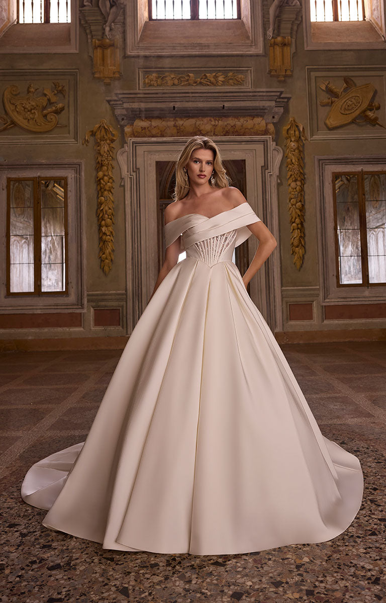 Woman in 63238A Aarti by Veni Infantino - Off-the-Shoulder Lace Ball Gown with Corset Back standing in an ornate room.