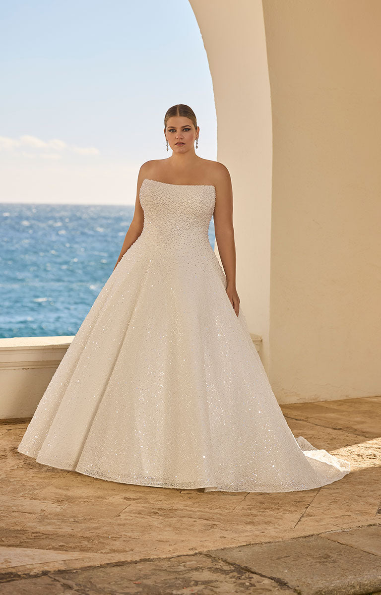 Woman in 63120 Hilani by Veni Infantino - Beaded Pearl Embellished Wedding Dress with Delicate Button Detail standing by a coastal setting