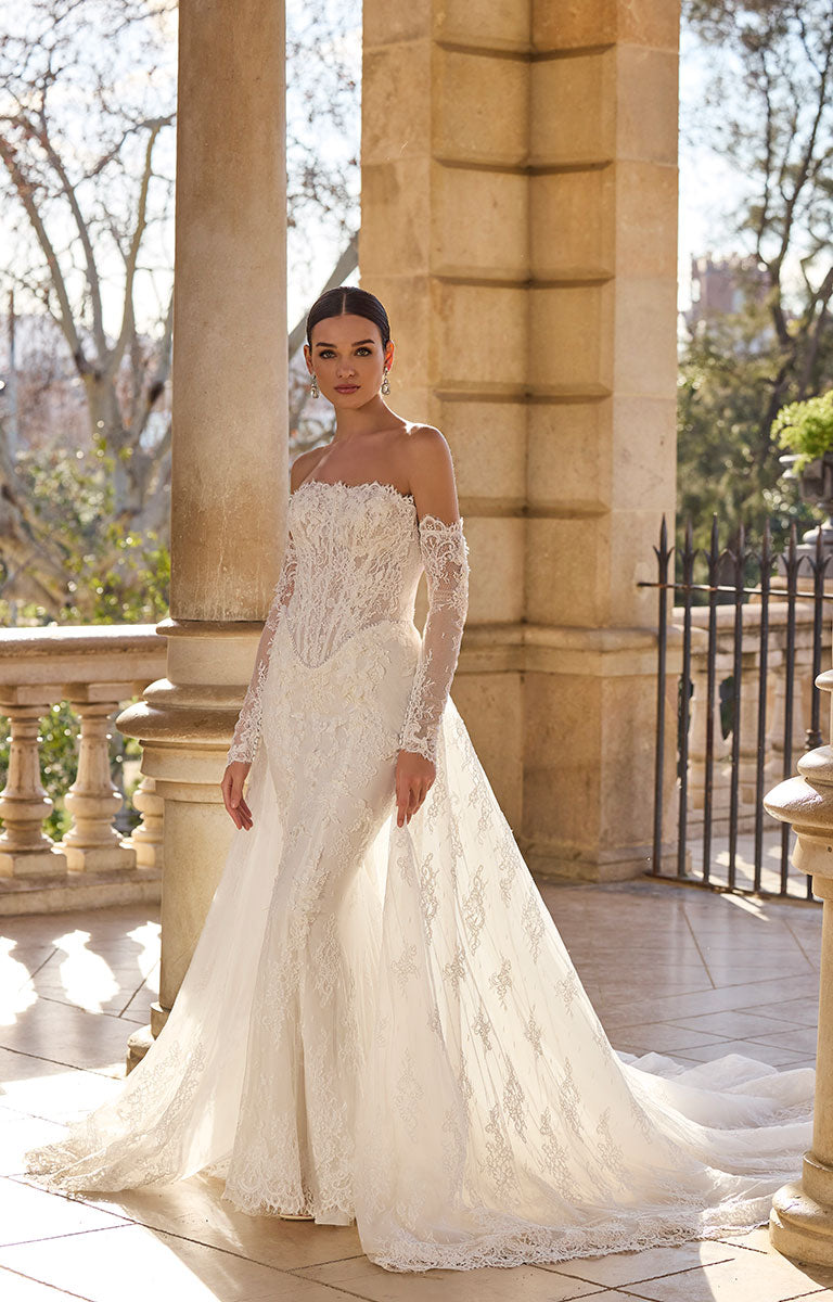 Woman in 63115A Hildred by Veni Infantino - Lace Wedding Dress with Romantic Silhouette standing outdoors with classical architecture.
