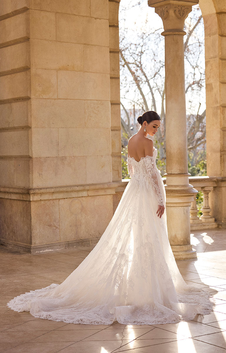 Woman in 63115A Hildred by Veni Infantino - Lace Wedding Dress with Romantic Silhouette standing in front of stone columns.