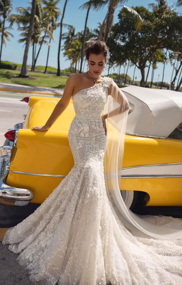 Woman in a white wedding dress standing next to a yellow vintage car with palm trees in the background.