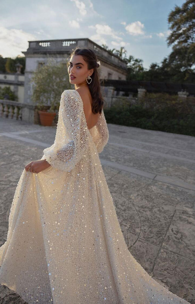 Woman in a sparkling white gown standing outdoors with a building and trees in the background