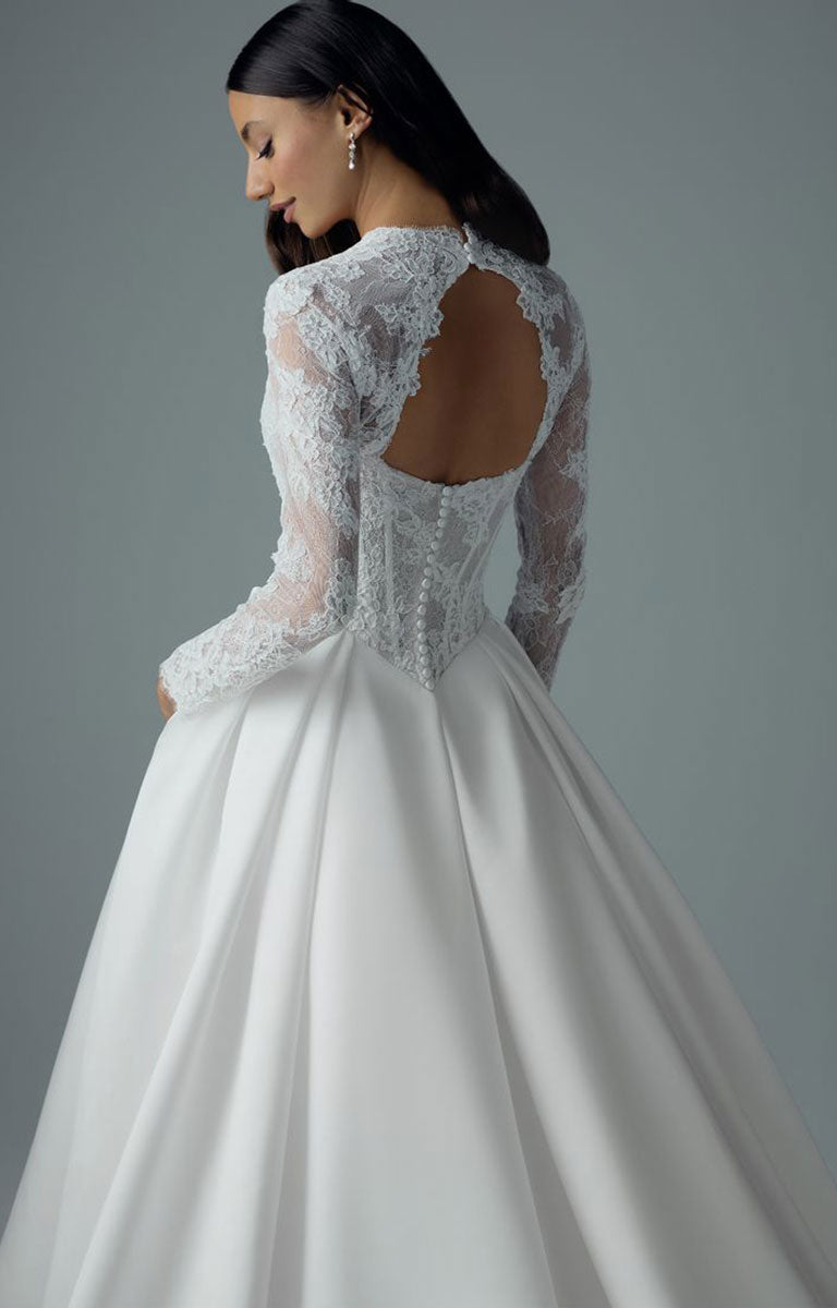 A woman wearing Bree Y3221 by Sophia Tolli - Corset Ball Gown Wedding Dress with Satin Skirt and Detachable Lace Jacket with long sheer lace sleeves, a fitted lace bodice, and a full satin skirt, shown from the back against a soft gray studio background.